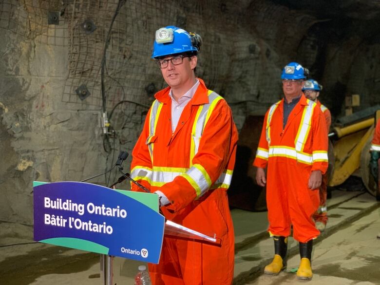 A man wearing orange coveralls standing at a podium that says, 'Building Ontario.'