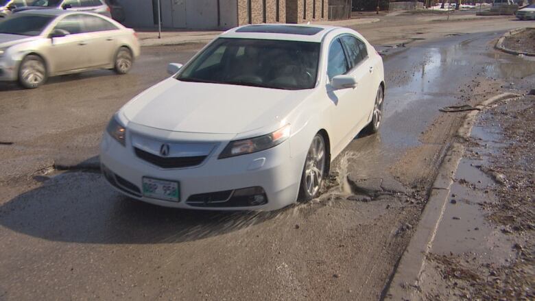 A white vehicle's front-right tire drives through a hole.