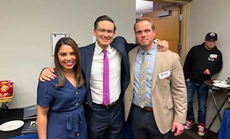 Three people in business attire stand with their arms around each other and grin for the camera.  