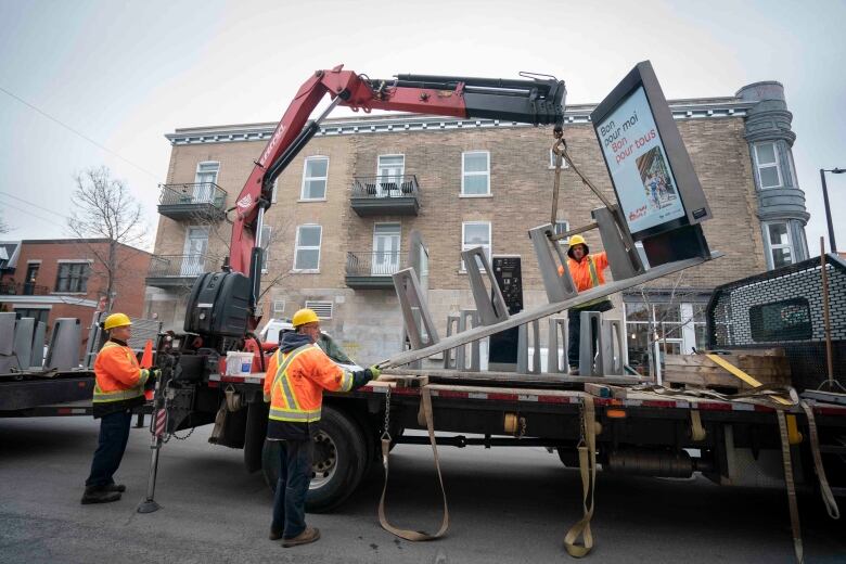 Workers wearing orange vests install a Bixi docking station on a street.