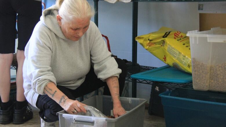 A woman scoops pet kibble from a bin. 