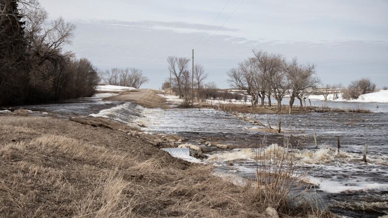 Spring flood waters pour over a gravel road into a ditch, filling up an adjacent field.