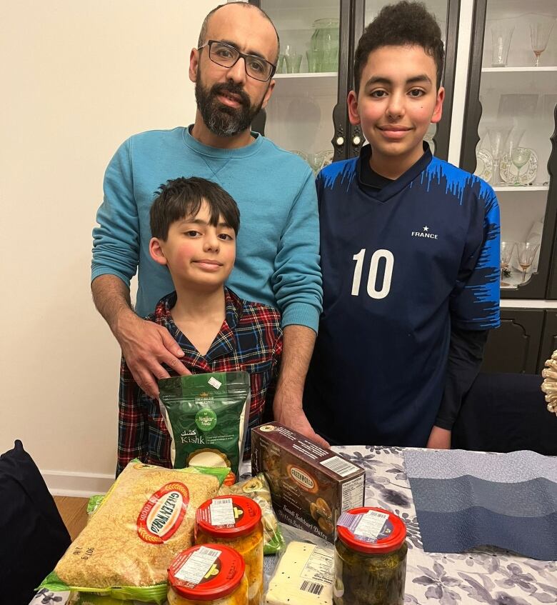 A man and two young boys pose with packages of food on the table. 