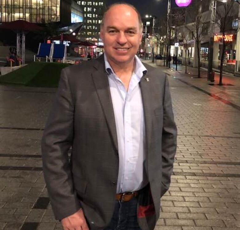 A man is on a street with lit up buildings in the background. 