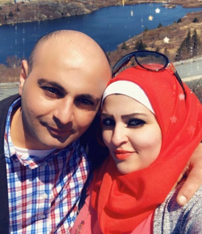 A man and a woman look at the camera with a pond in the backdrop. 