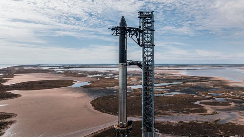 A silver and black rocket stands on a launch pad surrounded by marshes.