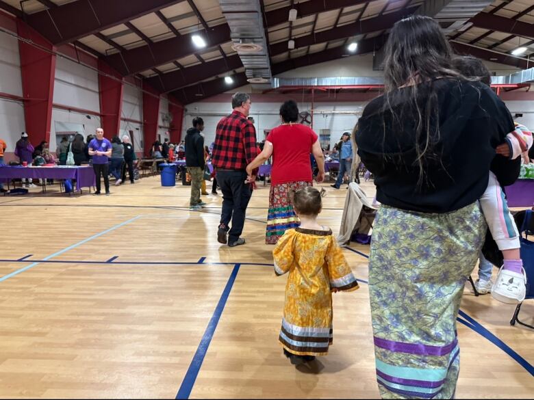 A young child in a yellow dress walks beside an older woman wearing a colourful, printed skirt.