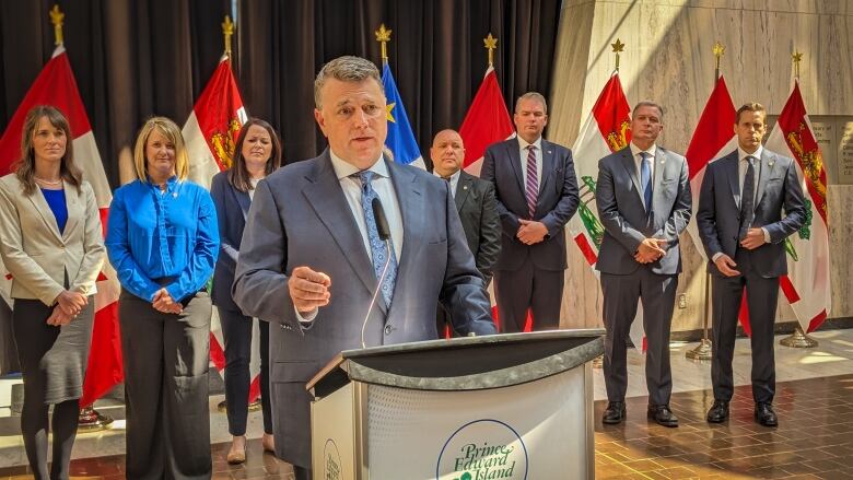 Man in business suit at the podium with formally dressed women and men behind him.