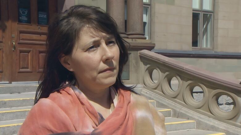 A woman with dark hair and a scarf stands outside Halifax City Hall