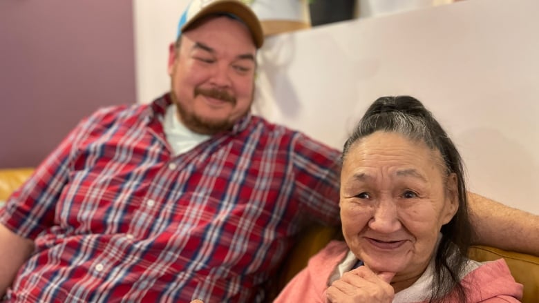 A man smiles at an older woman seated next to him on a couch.