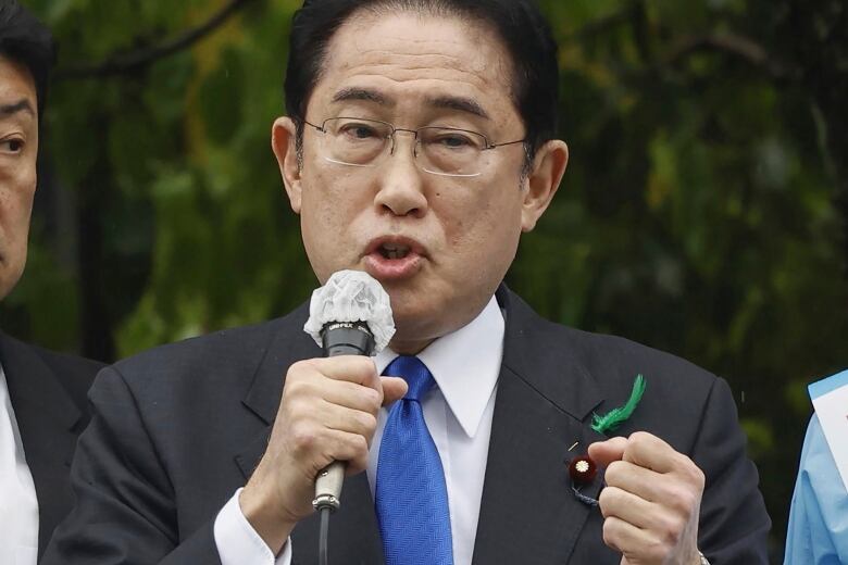 A man in business attire and a blue tie speaks into a microphone.