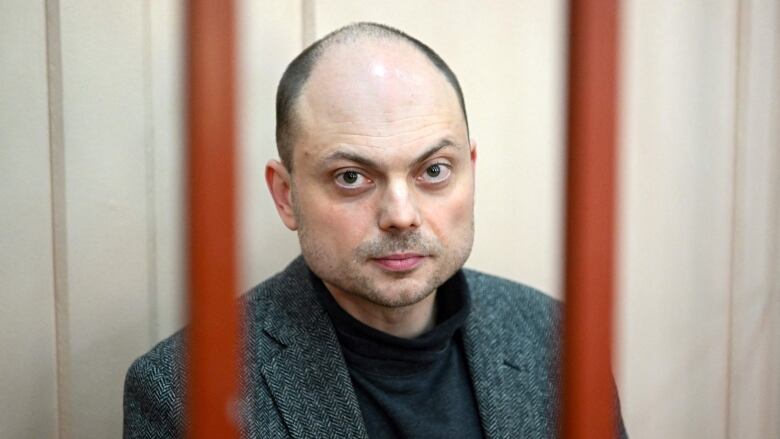 A balding man is shown in closeup behind bars.