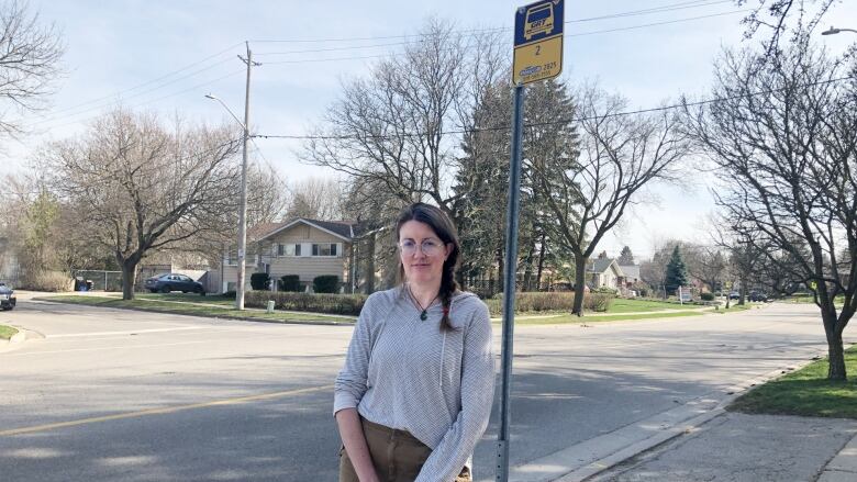 A woman stands underneath a bus sign in a suburban neighbourhood