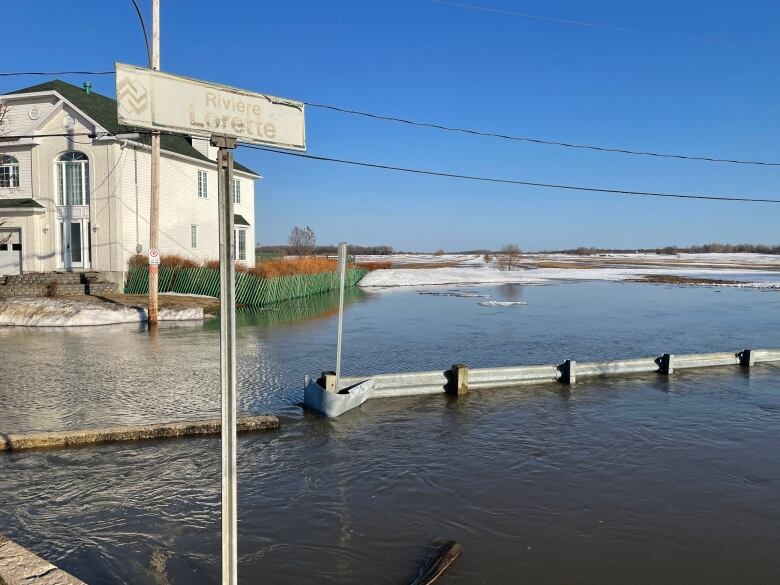 A flooded road near a home. Next to the home reads a sign Lorette River.