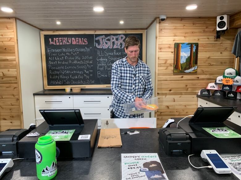 A man wearing a plaid shirt handles inventory inside a cannabis store.