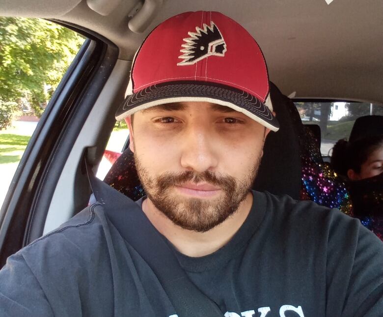 An Indigenous man sits with a red hat. 