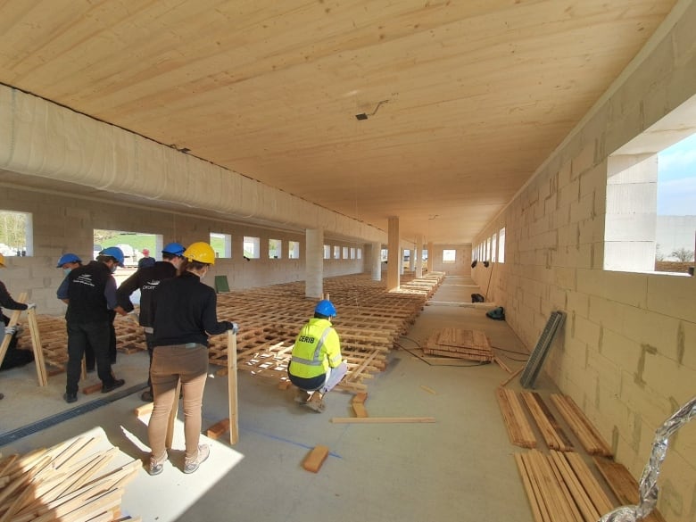 People wearing hard hats stack pieces of lumber on the floor of a large, cinderblock room to prepare for fire tests. 