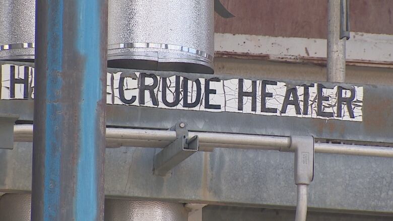 Pipes at a refinery are shown as well as a sign saying 'crude heater.'