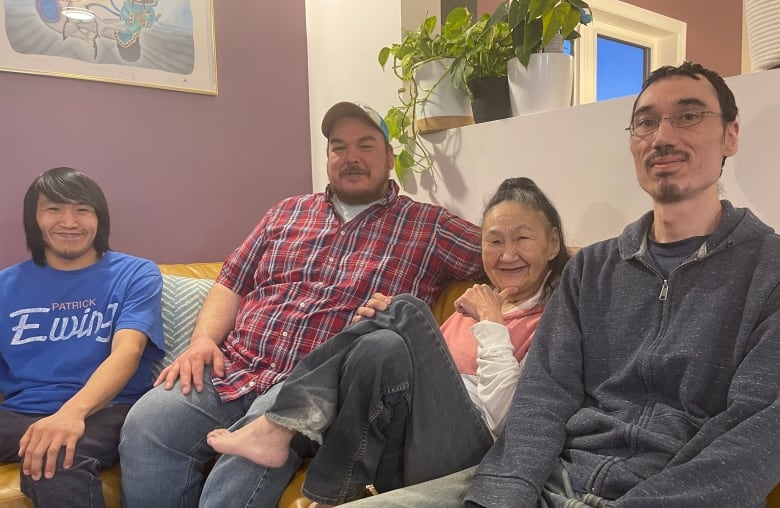 Three smiling men sit with a smiling woman on a sectional sofa. 