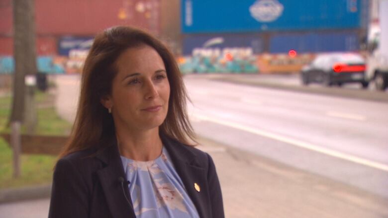 A woman looks to the camera as a freight train crosses a road and cars line up to wait.