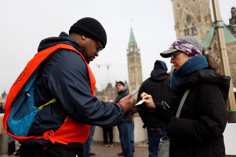 Someone in a orange vest scans someone's card using a device.