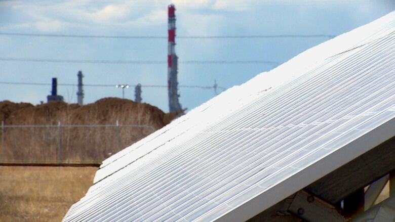 Solar panels are shown with an industrial facility in the background.