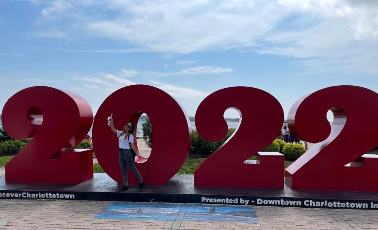 A woman wearing sunglasses poses in front of a giant red 2022 sign in front of the Charlottetown waterfront.