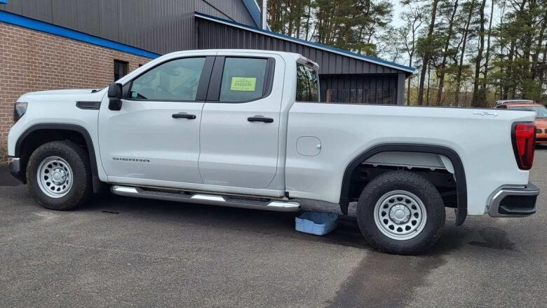 A white pickup truck sits in a parking lot with a blue container seen on the ground below.