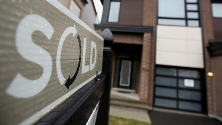 A 'sold' sign in front of a modern brown house.