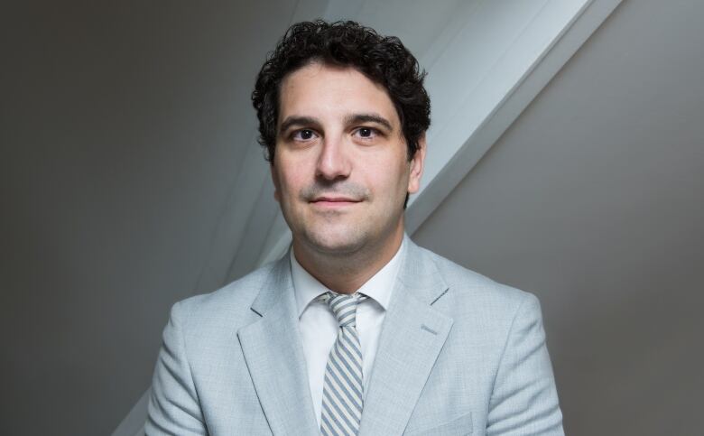 A man in a light grey suit and tie poses for a portrait.