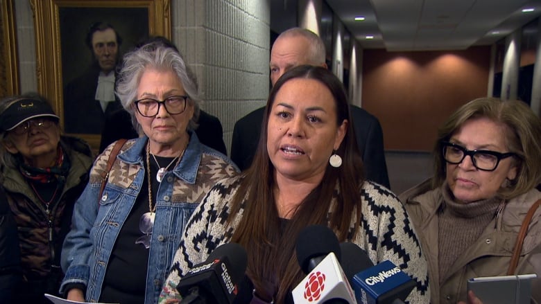 woman surrounded be people speaks into microphones