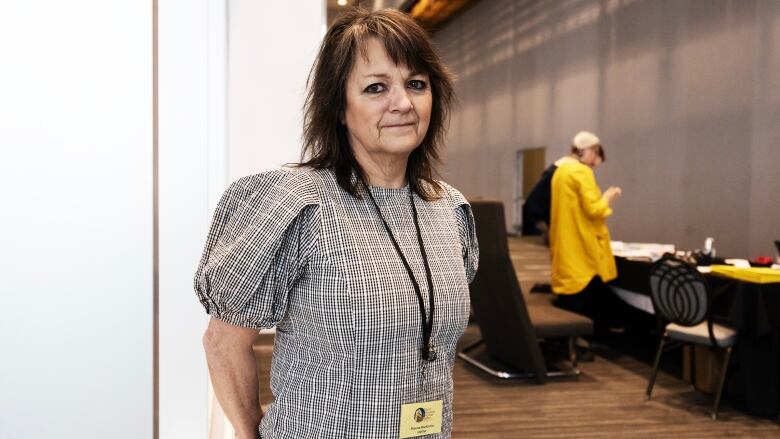 A woman wearing a lanyard is pictured in a large hallway outside of a conference room.