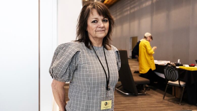 A woman wearing a lanyard is pictured in a large hallway outside of a conference room.