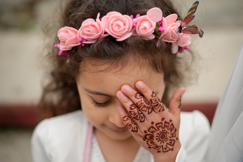 Close-up of a girl wearing peach-coloured flower headband, head tilted down and showing the back of her left hand decorated with henna.