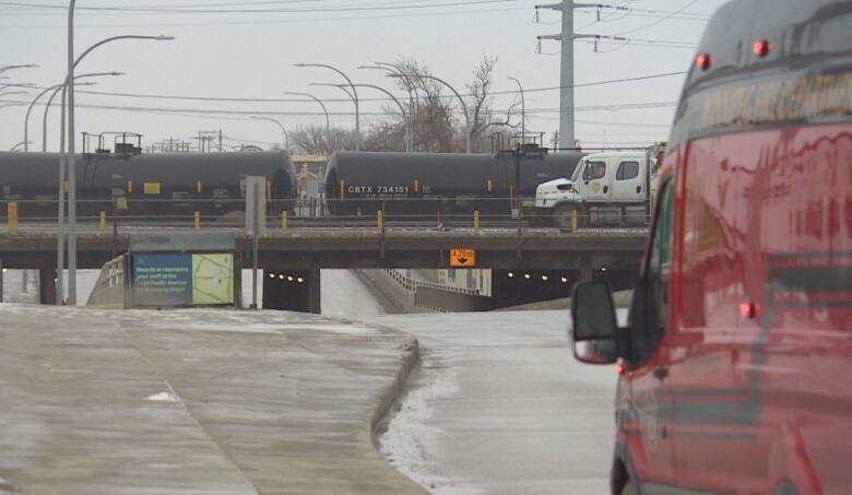 A red emergency vehicle is at right, the overpass with black tanker cars is in the background.