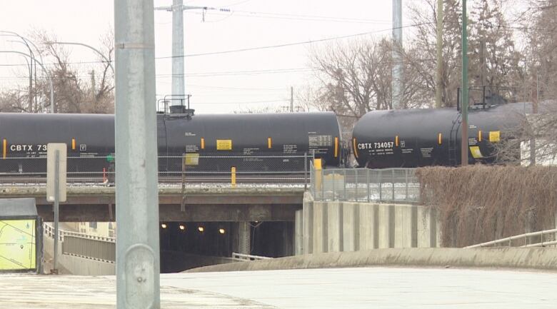 Black tanker cars that are part of the freight train are seen on the overpass.