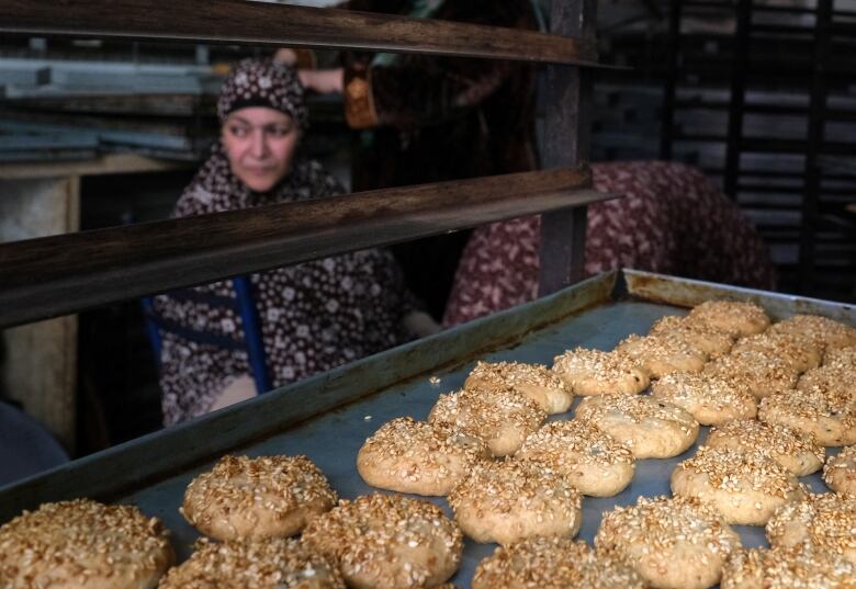 Women stand by a rack of baking sheets, including one featuring traditional butter cookies called kahk in Egypt, ahead of Eid.