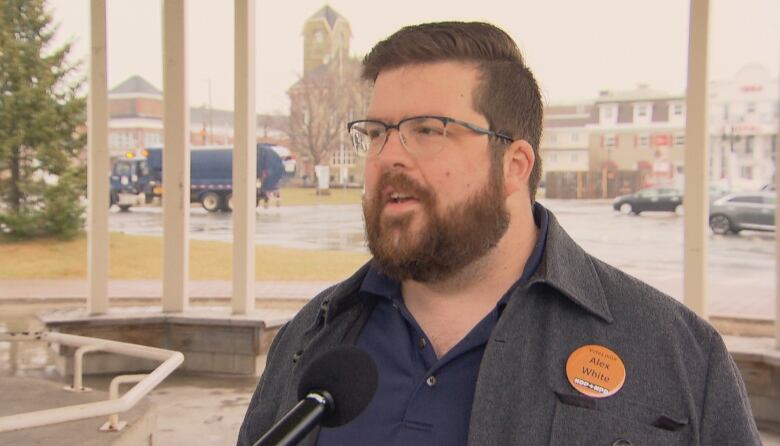 A bearded man with glasses speaking with a microphone in front of him.