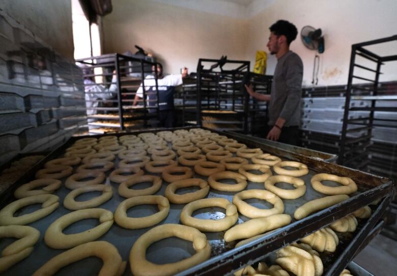 A worker is surrounded by racks of baking sheets with unbaked kahk traditional sweets, ahead of Eid.