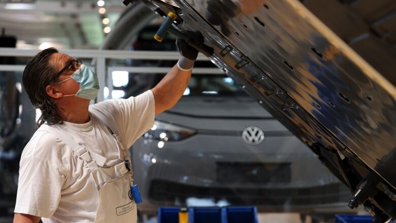 A man in a mask attaches a battery pack to the underside of a car