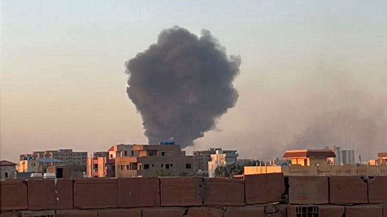 A plume of black smoke rises in the distance over a concrete apartment block.