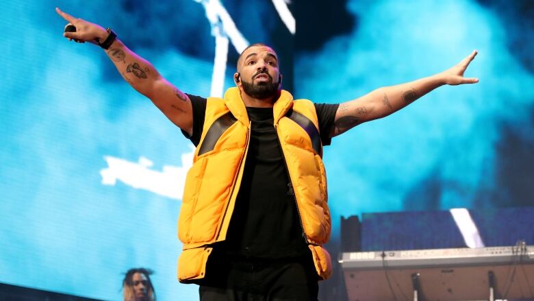 A man in a yellow vest stands in front of blue smoke on a stage. 