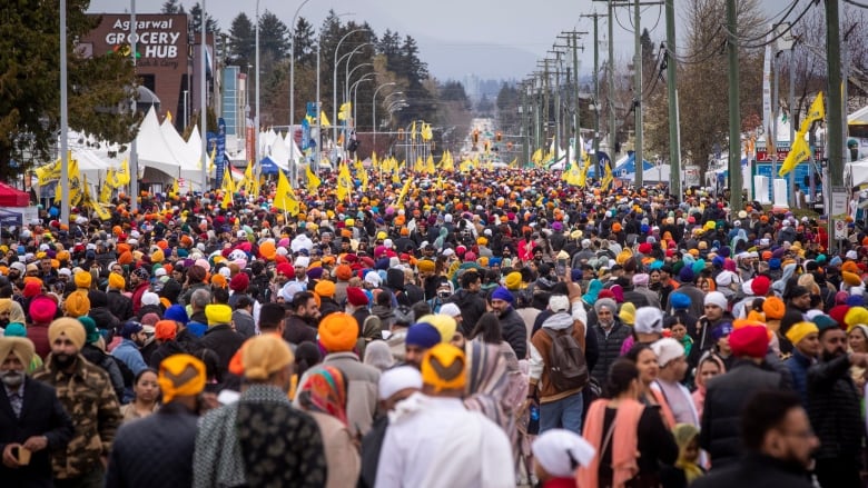 Thousands of people are pictured marching down a wide street, waving yellow flags. There are white tents on the side. 