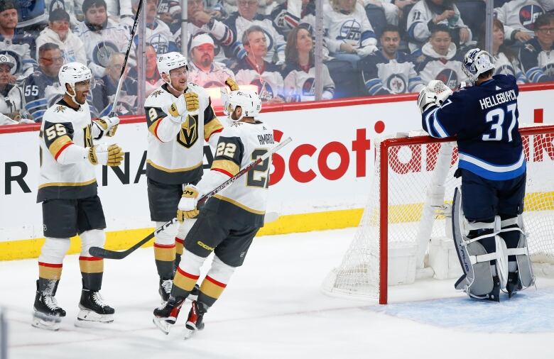 Three male ice hockey players smile while touching gloves as the opposing goaltender reaches for his water bottle on top of the net.