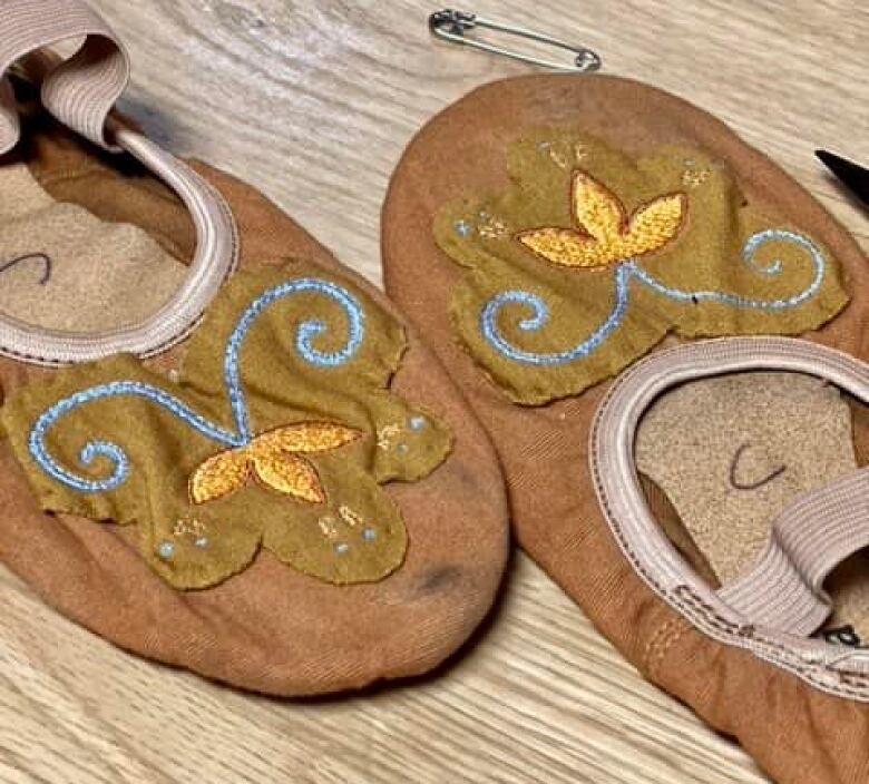 A pair of ballet shoes with blue double curves and gold florals. 