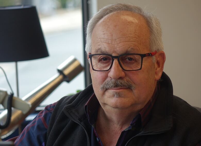 A man with grey hair and glasses in a dark vest and shirt.