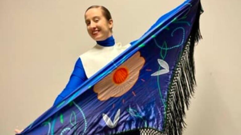 A dancer holds up a shawl with double curves and florals 