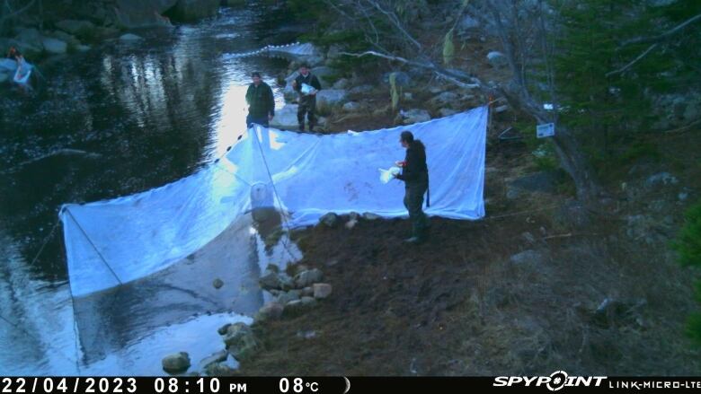 three men stand in front of a net in water.