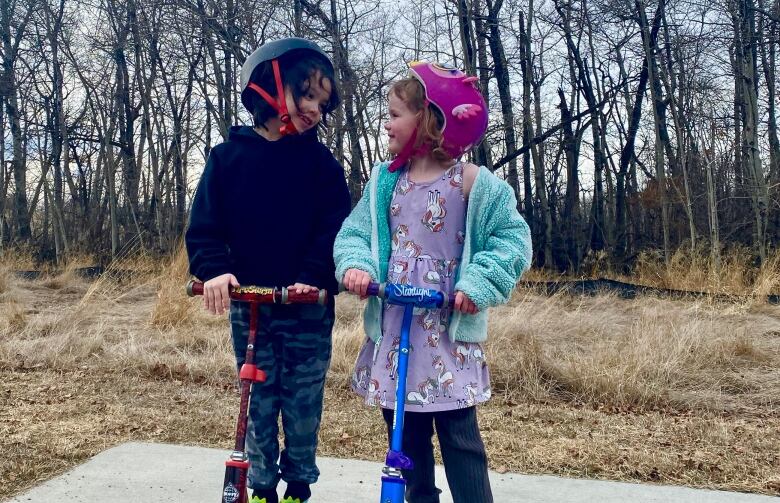 A boy and girl wearing bright coloured bike helmets smile at each other.