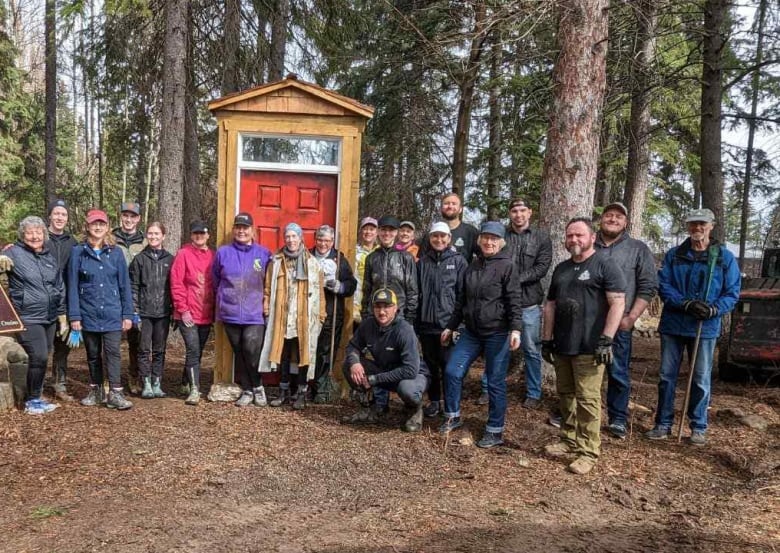 A group of people are picture being lined up in a woodland in front of a wooden door.